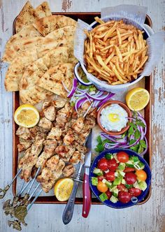 an assortment of food including chicken, fries and salad on a tray with utensils