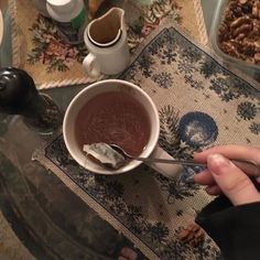 a person is holding a spoon over a bowl of chocolate and nuts on a table