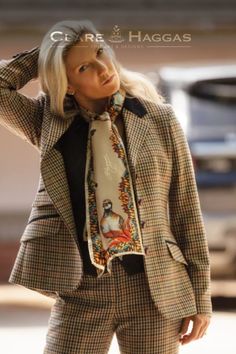 Woman in a plaid suit and colorful scarf, standing outdoors with her hand on her head.