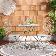 two chairs and a table on a rug in front of a brick wall with potted plants