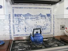 a blue tea kettle sitting on top of a gas stove next to a wall mural