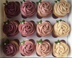 cupcakes with pink frosting and green leaves on top in a white box