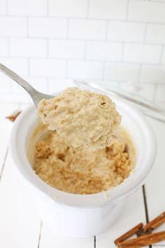 a spoon full of oatmeal in a white bowl with cinnamon sticks next to it