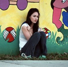 a woman sitting on the ground in front of a wall painted with cartoon character images