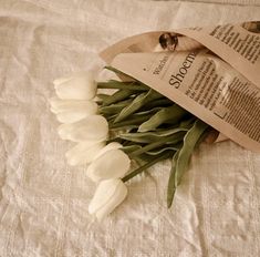 white tulips are laid out on a bed with a paper bag and tag