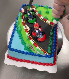 a person cutting into a birthday cake with mario kart on the front and sides