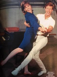 a man and woman are dancing together in front of a piano with their arms around each other