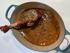 a pot filled with meat and beans on top of a white tablecloth covered table