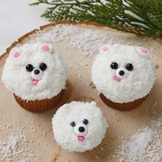 three cupcakes with white frosting and black eyes are on a wood slice