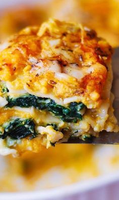 a piece of lasagna with spinach and cheese is being held by a fork