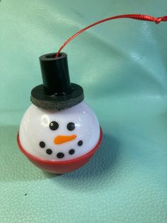 a snowman ornament hanging from a red string on a blue surface with a green background