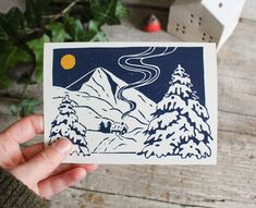 a person holding up a card with a mountain scene on it and trees in the background