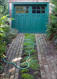 a green garage door with a hose connected to the side walk in front of it