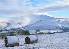 two hay bales are covered in snow on a snowy day with mountains in the background