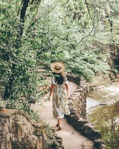 a woman wearing a straw hat walks along a path in the woods next to a river