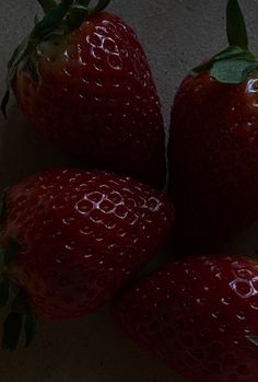 three red strawberries with green leaves on the top and bottom, sitting next to each other