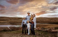 a family poses for a photo in front of a lake at sunset with the sun setting