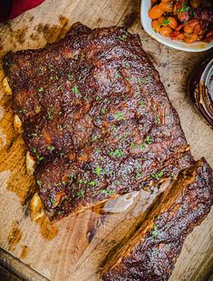 a large piece of meat sitting on top of a wooden cutting board next to a bowl of carrots