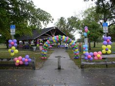 an arch made out of balloons in the middle of a park with picnic tables and benches