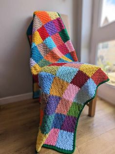 a colorful crocheted blanket sitting on top of a wooden chair next to a window