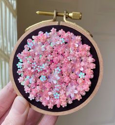 a hand holding up a small embroidery hoop with pink and blue flowers on it