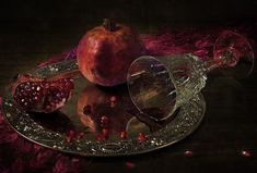 two pomegranates on a glass plate with a wine goblet