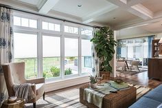 a living room filled with furniture and lots of windows covered in shades of green plants