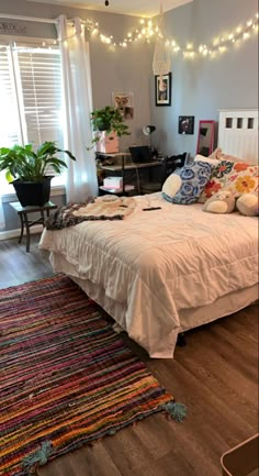 a bed sitting in a bedroom next to a window filled with plants and pillows on top of a wooden floor