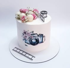 a white cake with pink flowers and film reel on top, sitting on a plate