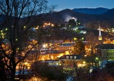 a city lit up at night with lights on the buildings and mountains in the background