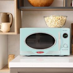 a microwave oven sitting on top of a counter next to a bowl of popcorn and a cup