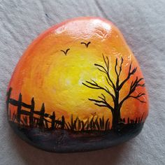 a painted rock with a tree and fence in the background at sunset on a paper towel