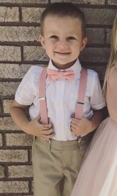 two young children standing next to each other in front of a brick wall wearing pink suspenders and bow ties