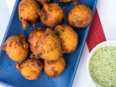 some fried food is on a blue plate next to a bowl of green dipping sauce