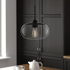 a glass light hanging over a wooden table in a room with black walls and cabinets