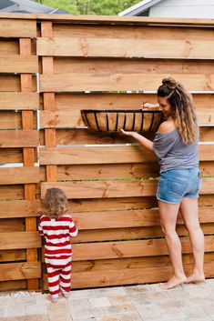 a woman holding a basket next to a little boy in front of a wooden fence