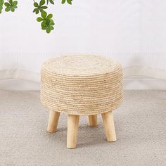 a small stool made out of straw with wooden legs on carpeted floor next to plant