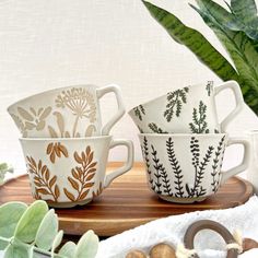 three coffee cups sitting on top of a wooden tray next to a potted plant