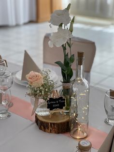 the table is set with white flowers and wine bottles on it, along with place cards