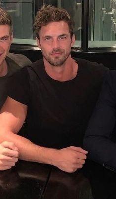 two men are sitting at a table with their arms crossed and one man is wearing a black shirt