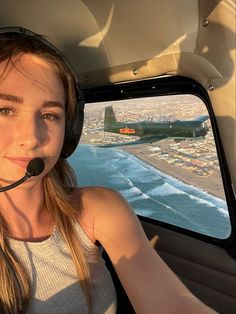 a woman wearing a headset in the cockpit of an airplane flying over a city