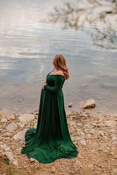 a pregnant woman in a green dress standing on rocks near the water's edge