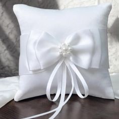 a white pillow with a bow on the side and ribbon at the end, sitting on a table