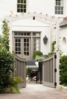 an open gate leading to a white house with potted plants on either side and a table in the middle