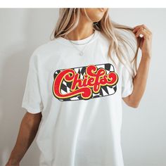 You will love this super cute and cozy Kansas City Chiefs shirt! This is a unisex fit t-shirt, made with direct to film transfer, no vinyl or sublimation is used.  T-shirts are comfort colors soft washed garment-dyed tees, renowned for their softness, comfort, and durability. Made with 100% ring-spun cotton, and sure to make an excellent choice for comfortable daily wear. T-shirts have double needle stitching throughout, sewn in twill label, and ribbed collar.  In order to provide the most color choices, sweatshirts in Pepper and Ivory are made using Comfort Colors 100% soft ring-spun cotton, while sweatshirts in white, black, grey, red, and sand are made using Gildan Cozy Feel, 50% cotton 50% poly blend. Both have a ribbed collar and relaxed fit and will make a great addition to your game Kc Chiefs Shirts Vinyl, White Cotton Sublimation T-shirt With Funny Print, White Pop Culture Shirt With Letter Print, Pop Culture Relaxed Fit Shirt With Letter Print, Pop Culture Graphic Print Shirt With Relaxed Fit, Pop Culture Short Sleeve Shirt With Letter Print, Funny Print Graphic Tee, Relaxed Fit Graphic Tee With Sublimation Design, Trendy Crew Neck Sublimation T-shirt With Screen Print