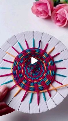 someone is holding up a paper plate with yarn on it and pink roses in the background