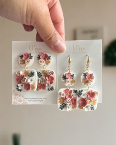 a pair of earrings is being held up by a person's hand, with the image of flowers on them