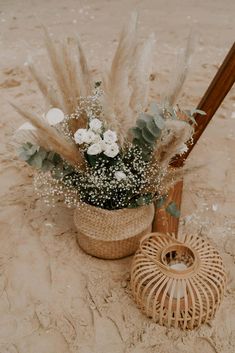 a basket filled with flowers next to an umbrella on top of a sandy beach covered in sand