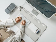 a woman is typing on her computer at the desk with an apple monitor and keyboard