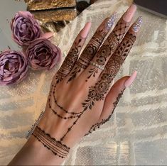 a woman's hand with henna tattoos on it and flowers in the background